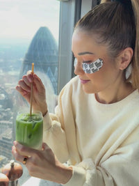 Dr. Luise Berger mit den DOC BERGER EFFECT Glowing Eye Patches und Matcha vor Skyline für die perfekte Augenpflege auf Reisen gegen Schwellungen, Augenringe und müde Haut unter den Augen