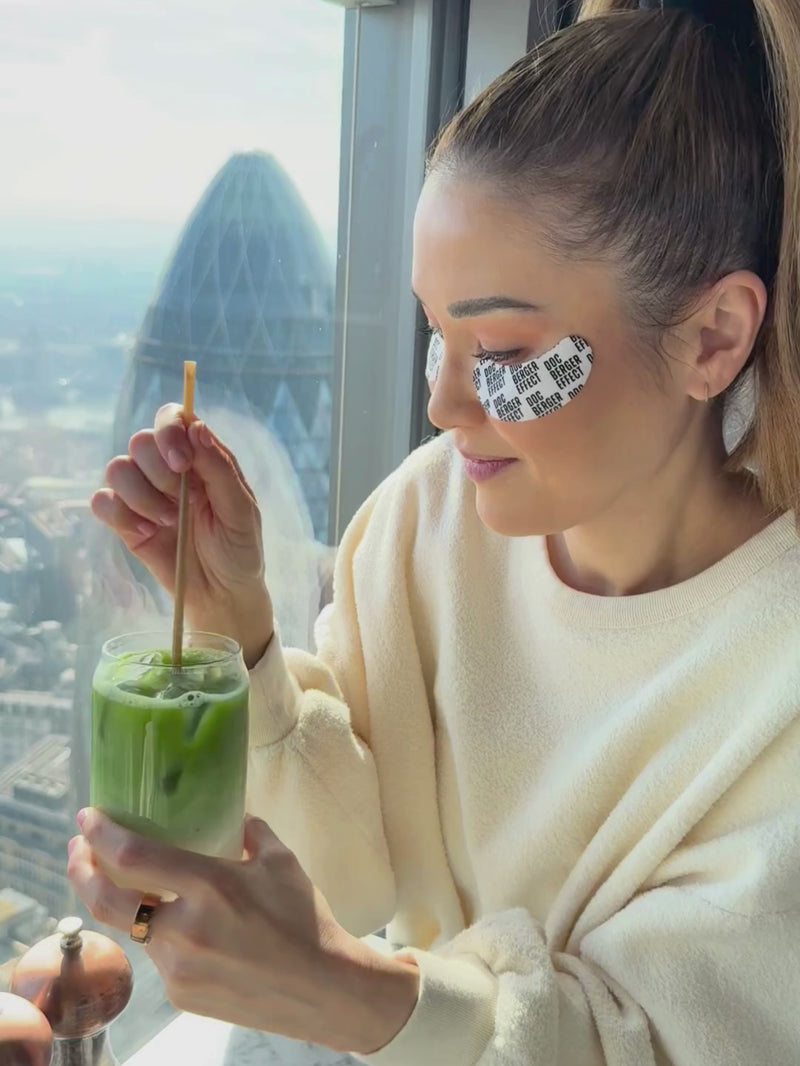 Dr. Luise Berger mit den DOC BERGER EFFECT Glowing Eye Patches und Matcha vor Skyline für die perfekte Augenpflege auf Reisen gegen Schwellungen, Augenringe und müde Haut unter den Augen